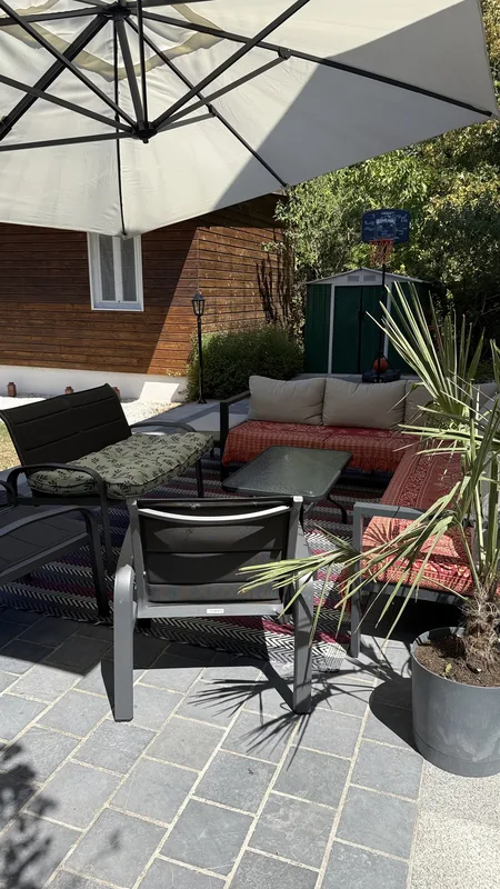 Salon de jardin sous un grand parasol avec panier de basket et cabane de rangement au fond
