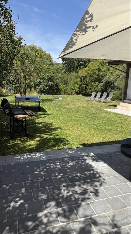 Vue du jardin avec table de ping-pong, transats et pelouse depuis la terrasse ombragée