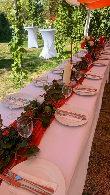 Table dressée avec chemin de table rouge, fleurs et bougies sous le chapiteau