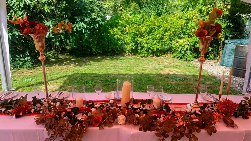 Table dressée avec compositions florales orange et bougies devant la pelouse