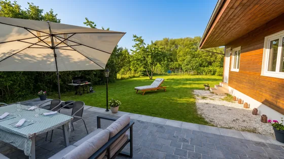 Terrasse avec table à manger, parasol, salon de jardin et vue sur la grande pelouse arborée
