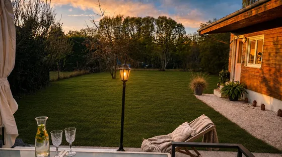 Jardin au coucher du soleil avec transat, rideau voilage, lampadaire et bougies sur le rebord de la dépendance