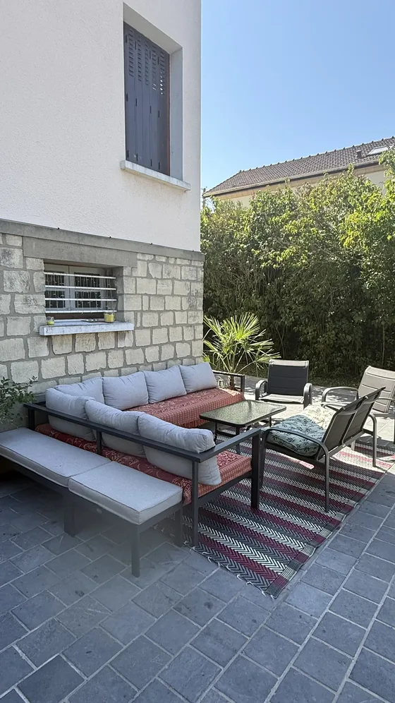 Salon de jardin avec canapé, table basse et fauteuils sur la terrasse contre la façade en pierre