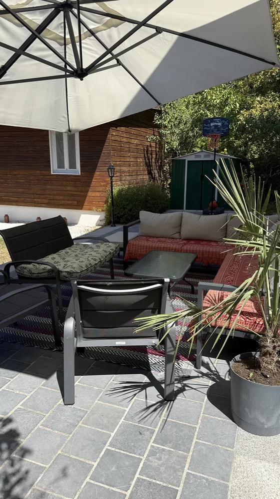 Salon de jardin sous un grand parasol avec panier de basket et cabane de rangement au fond