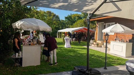 Bar à cocktails sous parasol avec invités dans le jardin et chapiteau en arrière-plan