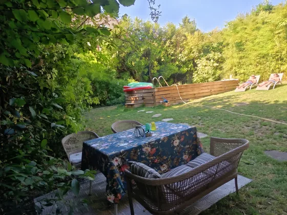 Table dressée et fauteuils en osier sur la terrasse ombragée face à la piscine de Sarcelles
