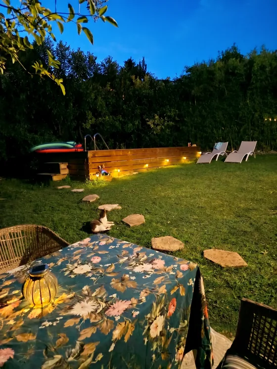 Jardin de Sarcelles illuminé le soir, table dressée et piscine éclairée au coucher du soleil